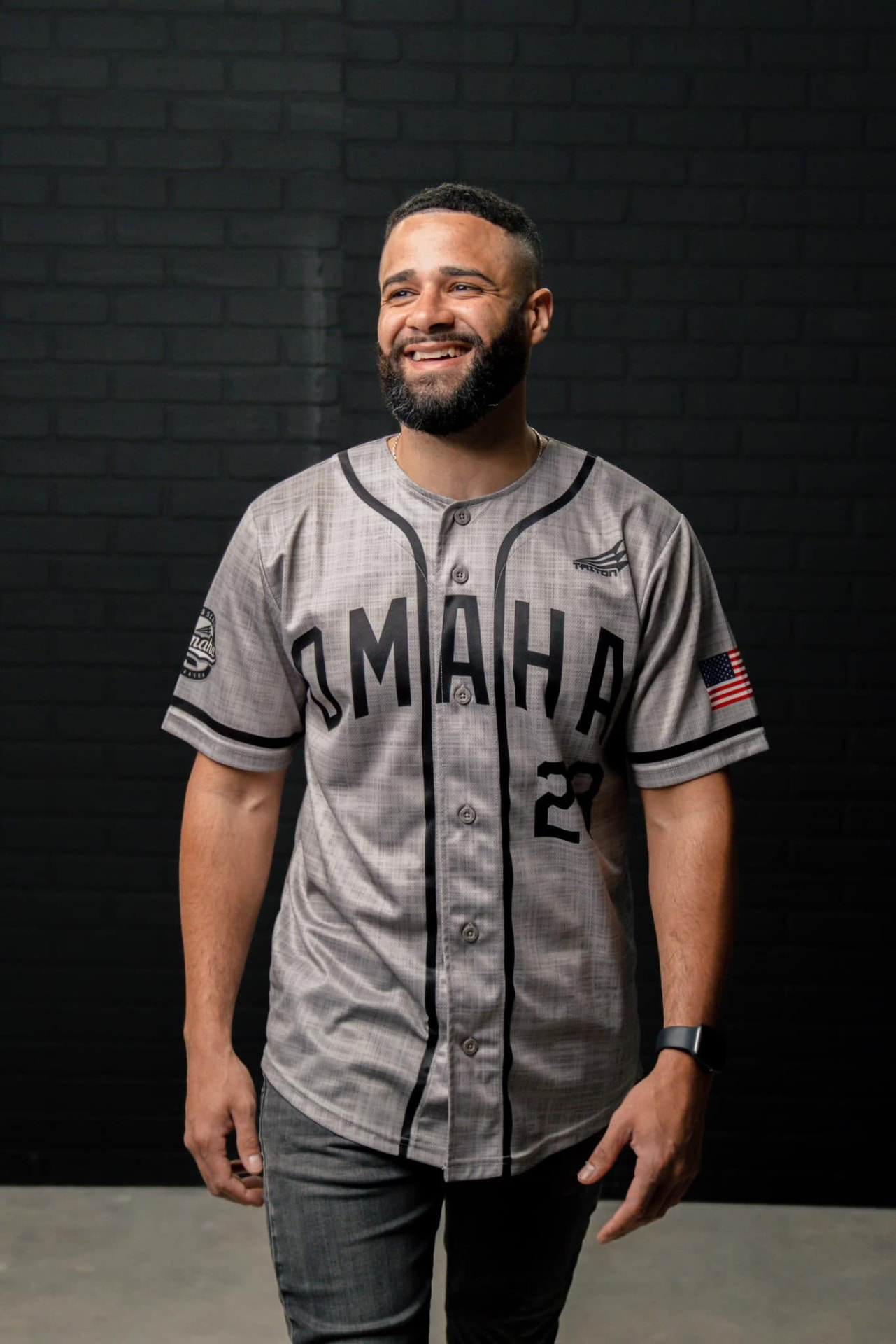 Devon Dupree smiling in an Omaha baseball jersey against a dark brick wall