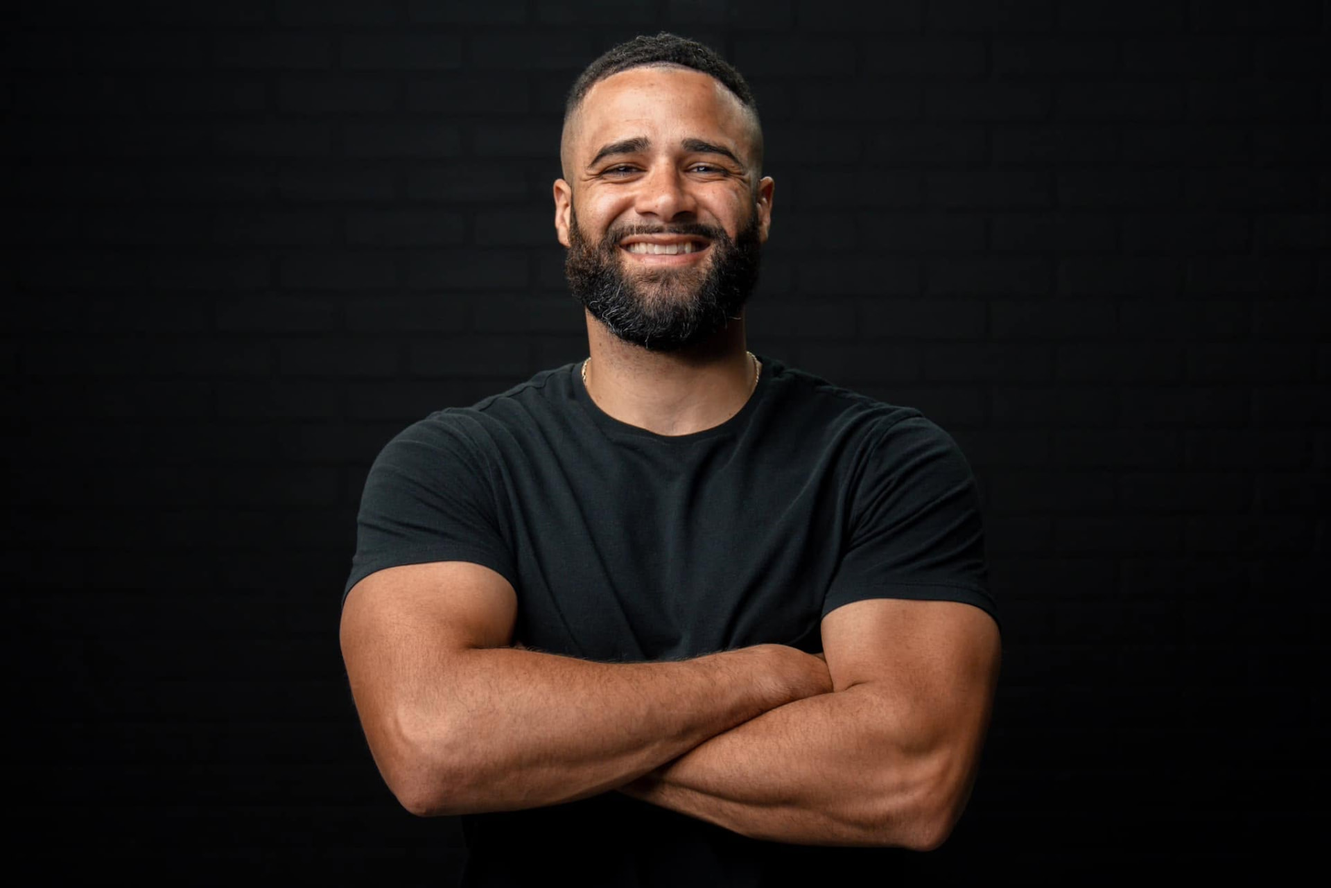 Studio portrait of Devon Dupree in a black t-shirt against a dark brick wall